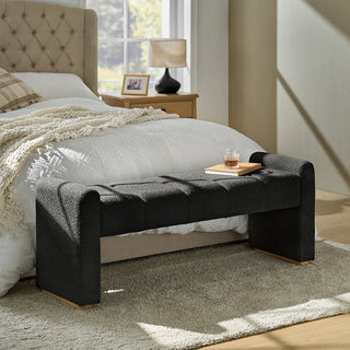 Black boucle ottoman positioned at foot of bed in modern bedroom showing practical application