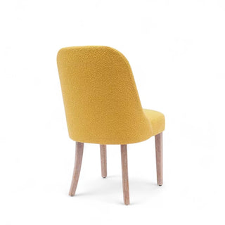 Angled back view showing the boucle texture and tapered wooden legs of the chair.
