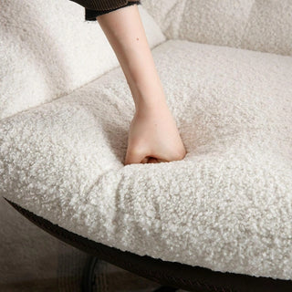 Hand pressing into the thick white boucle cushion of the lounge chair, highlighting its soft texture.