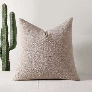 Beige boucle pillow cover with gentle texture, styled with greenery in the background.