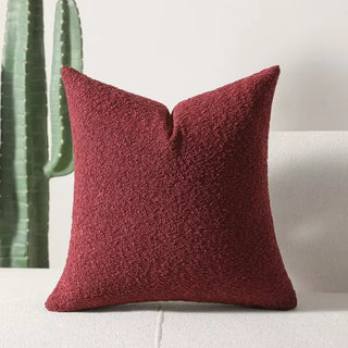 Burgundy red boucle pillow cover standing upright with cactus accents in the background.