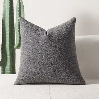 Dark grey boucle pillow cover providing contrast on a pale seating surface.