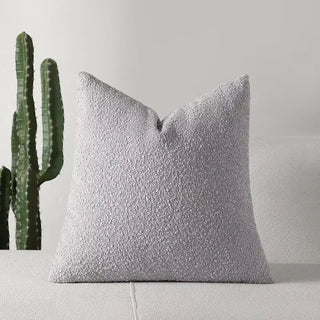 Soft light grey boucle pillow cover on a white couch, styled in minimalist decor.