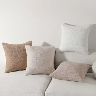 Assorted boucle pillow covers in ivory, camel, and grey displayed on a neutral sofa.