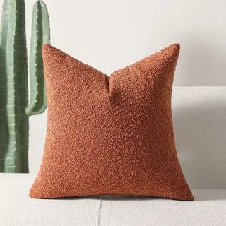 Deep rust-colored boucle pillow cover placed upright with cactus decor in the background.