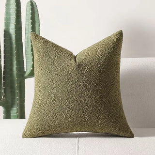Sage green boucle pillow cover displayed on a light beige couch with a cactus plant in the background, showcasing its textured surface and plush feel.
