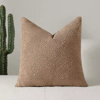 Warm camel-toned boucle pillow cover styled with natural decor elements.