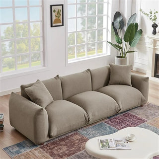 Mocha boucle sofa styled in bright living room with large windows, decorative throw pillows, hardwood flooring, colorful patchwork area rug, white coffee table, and indoor plant creating an inviting mid-century modern space