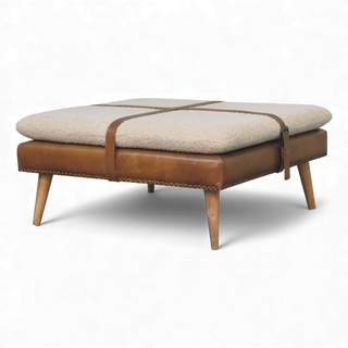 Beige ottoman with brown leather straps and wooden legs on a white background