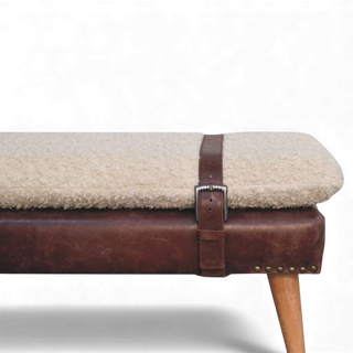 Close-up of the cream bouclé bench showing the brown buffalo leather strap and belted accent wrapped around the cushioned seat edge.