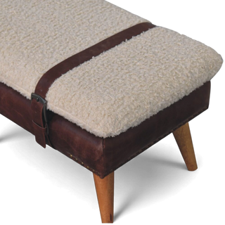 Close-up angled view of the cream bouclé seat surface with a brown buffalo leather strap running across the top and over the side.