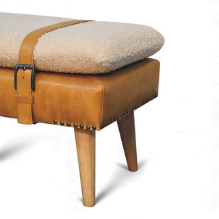 Beige cushioned ottoman with brown leather strap and wooden legs on a white background