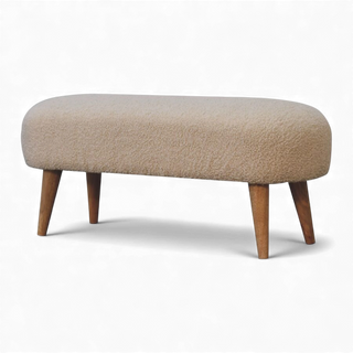 Angled view of a beige bouclé bench featuring soft curves, smooth upholstery, and natural wooden legs.
