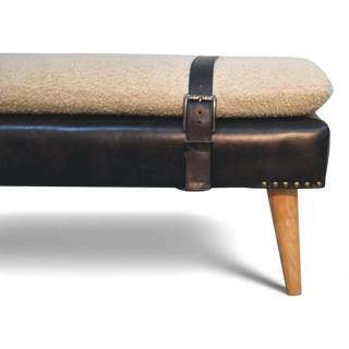 Beige cushioned bench with black leather strap and wooden leg on a white background