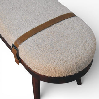 Round ottoman with textured beige surface and brown leather strap on a white background