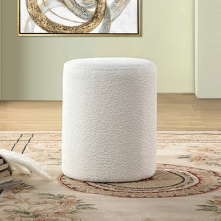White boucle ottoman placed in living room with light green walls and natural decor