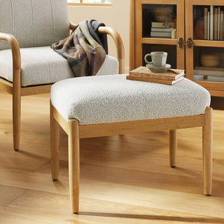 White boucle ottoman placed in living room with wooden furniture and decor elements