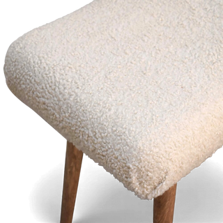 Three-quarter angled view of the Bouclé Bench Cream Curved Nordic from the right side with the sculpted seat and wooden legs.


