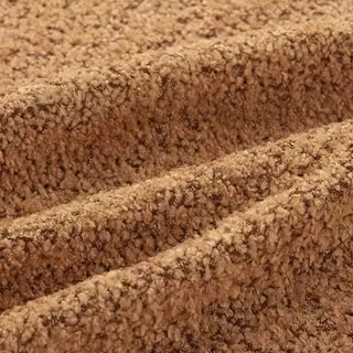 Close-up of camel brown bouclé fabric showing three diagonal folds, highlighting its plush, nubby texture