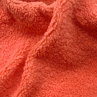 Close-up of orange teddy fabric highlighting its soft, fluffy surface texture.