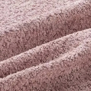 Close-up of blush pink bouclé fabric showing three diagonal folds, featuring its characteristic nubby, looped texture.