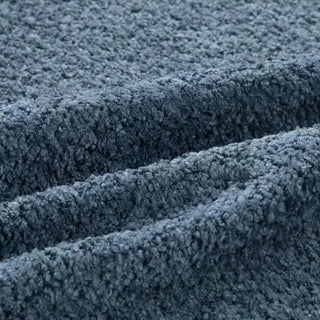 Close-up of slate blue bouclé fabric with diagonal folds, highlighting its textured surface.